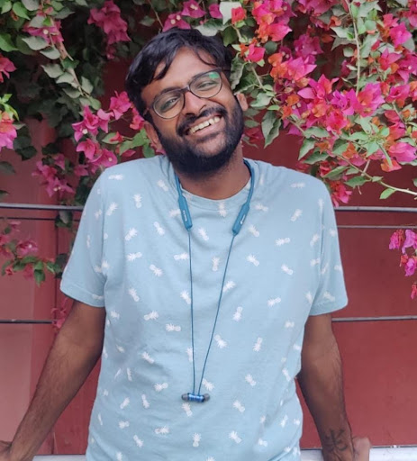 A picture of Chand posing in front of a wall of flowers